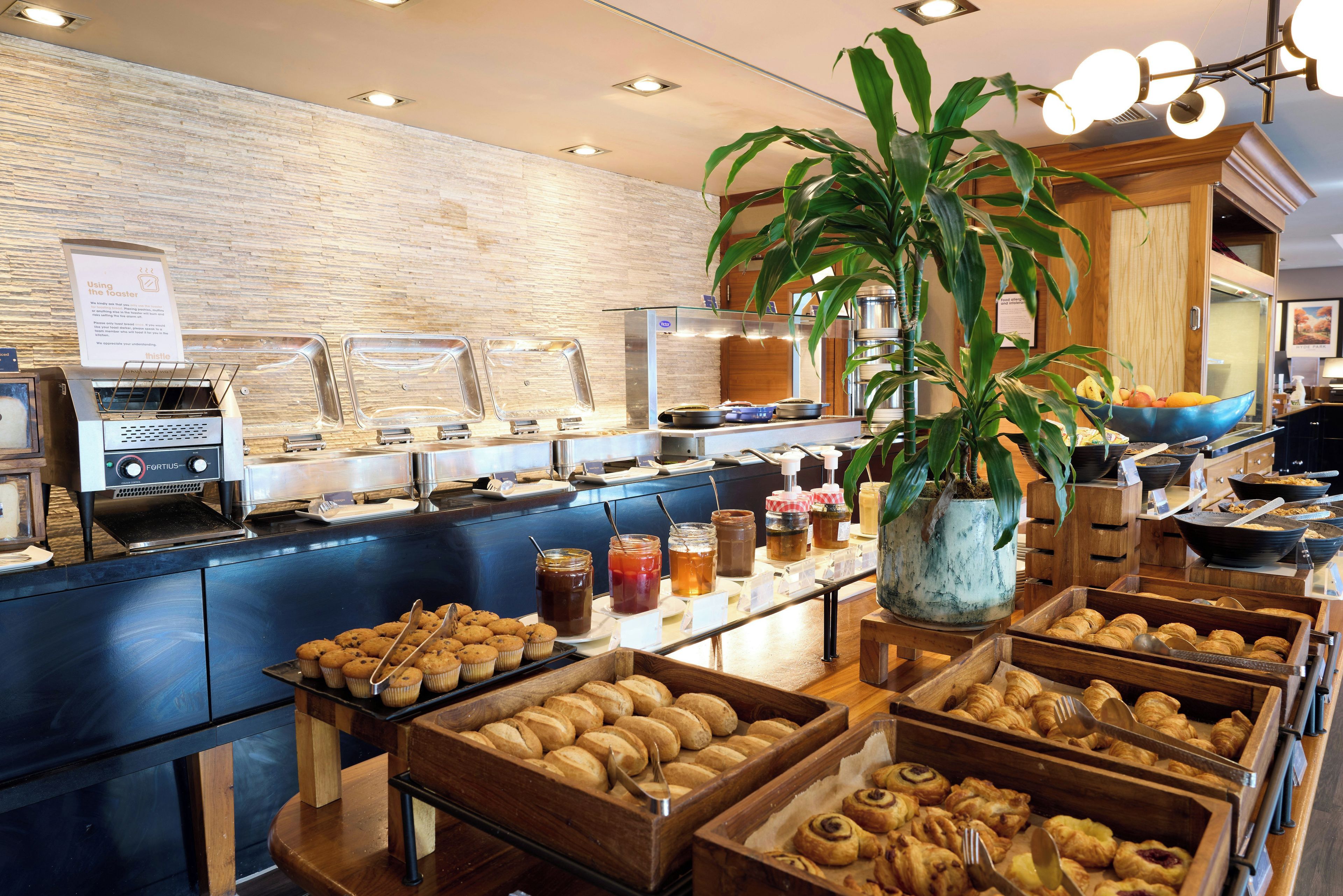 A buffet area with various food items, a coffee machine, and a large potted plant.