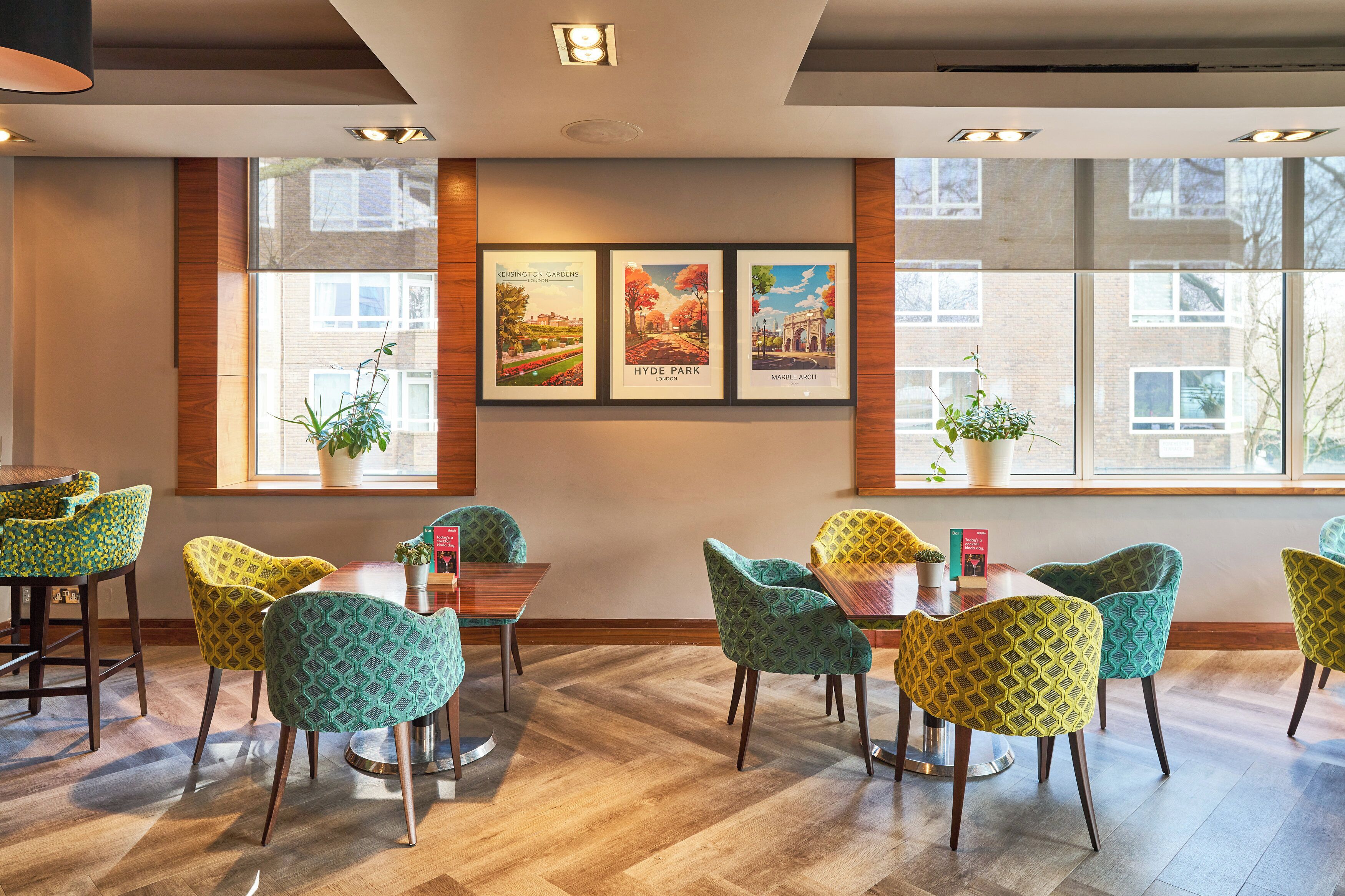 A dining area with wooden flooring, green patterned chairs, and framed pictures on the wall.