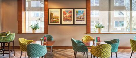 Un espace repas doté d’un plancher en bois, de chaises à motifs verts et de tableaux encadrés accrochés au mur.