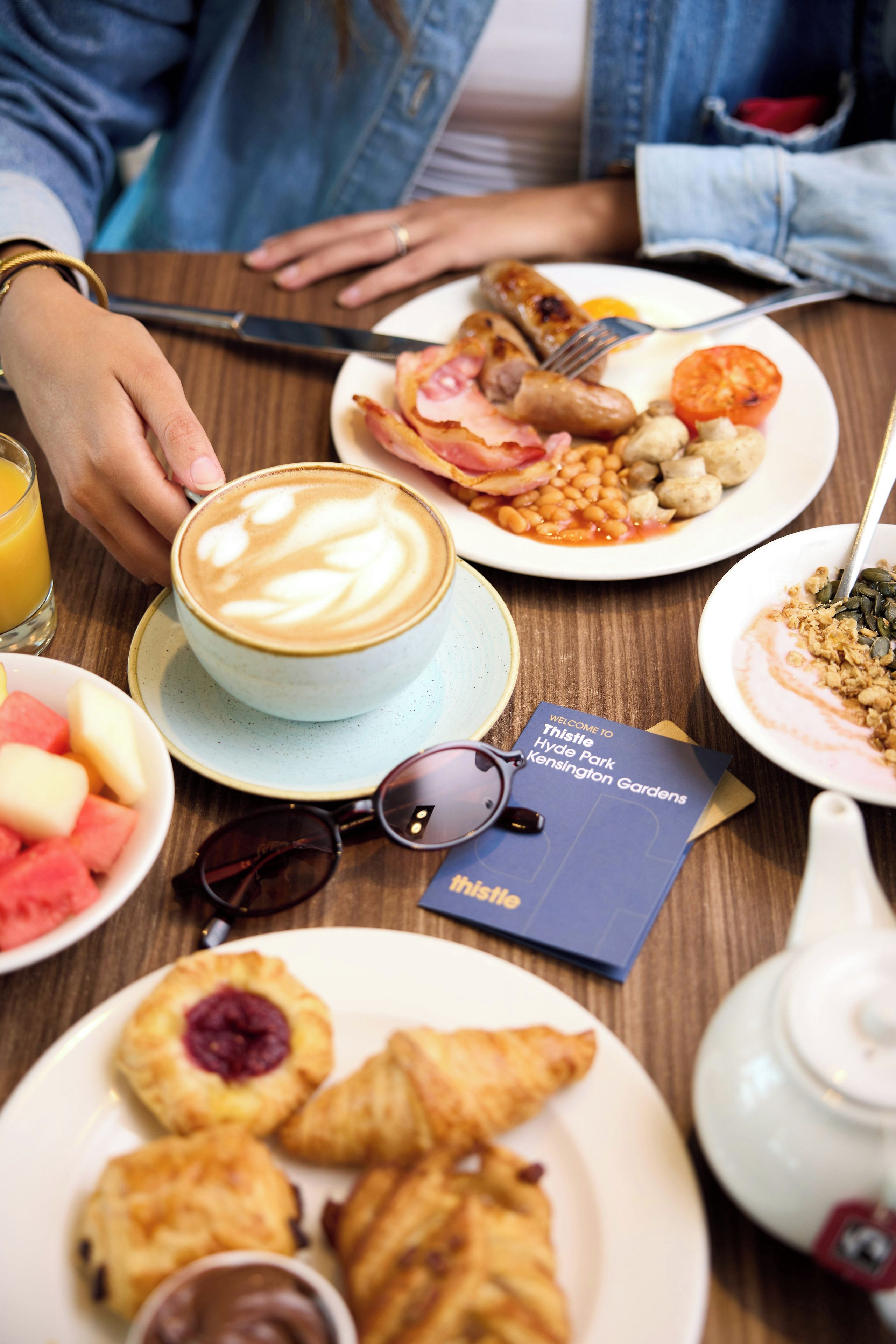 A table with a coffee cup, plates of food, a teapot, and a brochure.