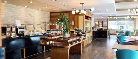 A modern hotel lobby with a buffet area, wooden reception desk, and seating with colorful chairs.