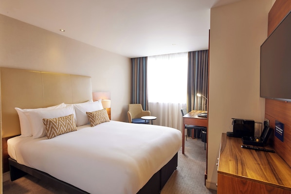 Une chambre d’hôtel avec un grand lit, un bureau, une chaise, une télévision et une fenêtre avec des rideaux.