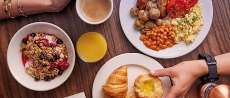 Desayuno dispuesto con platos de comida, una taza de café y un vaso de zumo de naranja sobre una mesa de madera.