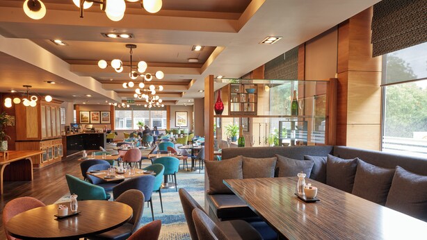 A modern restaurant interior with round tables, cushioned seating, and pendant lighting. - Thistle London Hyde Park Kensington Gardens (London)