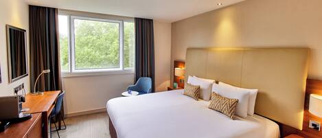 A hotel room with a large bed, a desk with a laptop, a chair, and a window with curtains.
