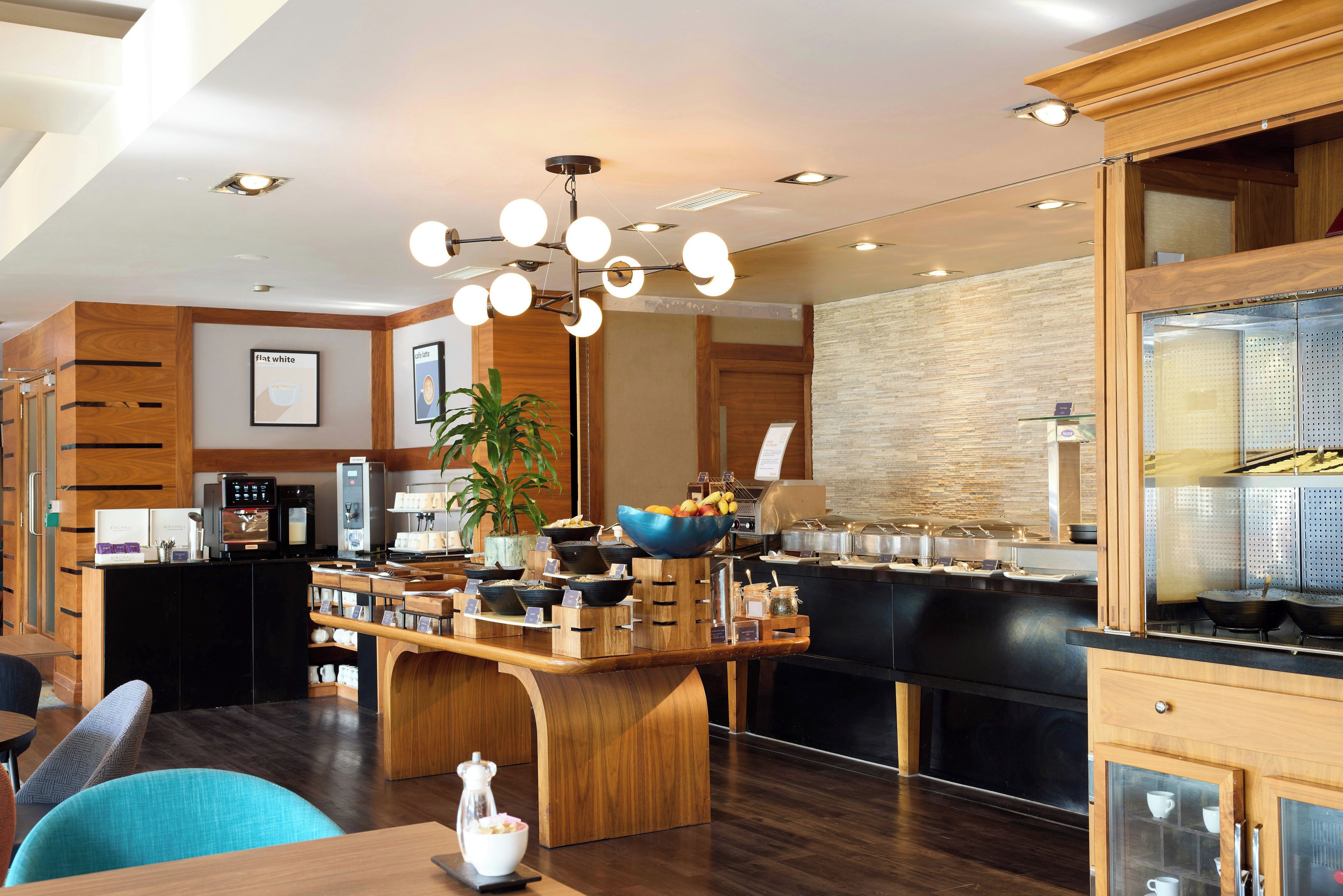 A modern hotel lobby with a coffee station, seating area, and a reception desk.