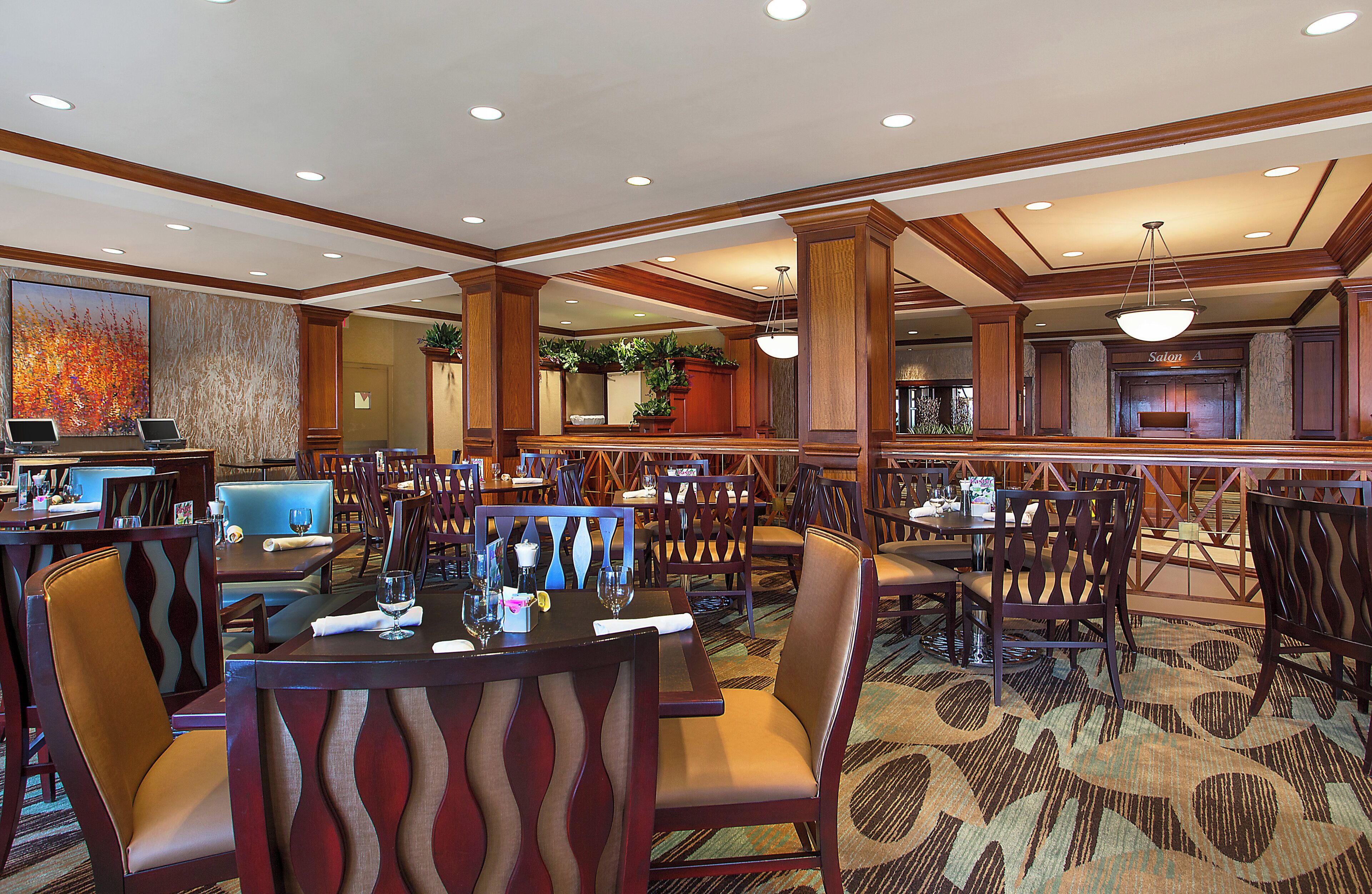 A hotel dining area with multiple tables and chairs, a reception desk, and a large painting on the wall.
