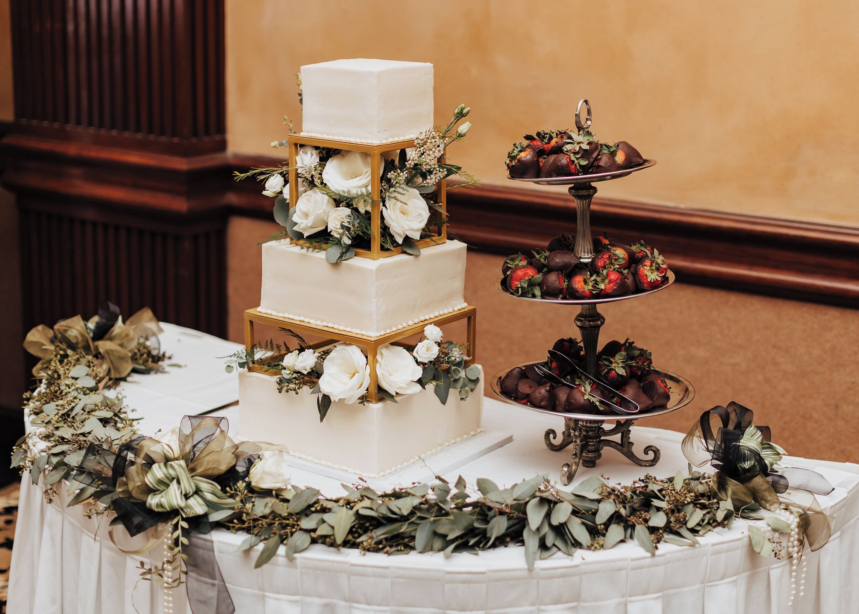 Pastís de noces de tres pisos decorat amb flors, envoltat d'una taula amb estovatge blanc i una varietat de postres.