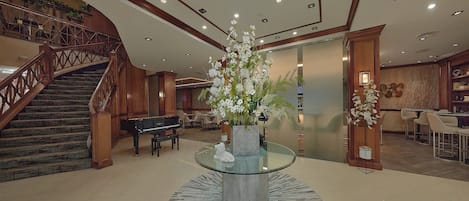 Un amplio vestíbulo con un piano, una escalera y una mesa central de cristal con un arreglo floral.