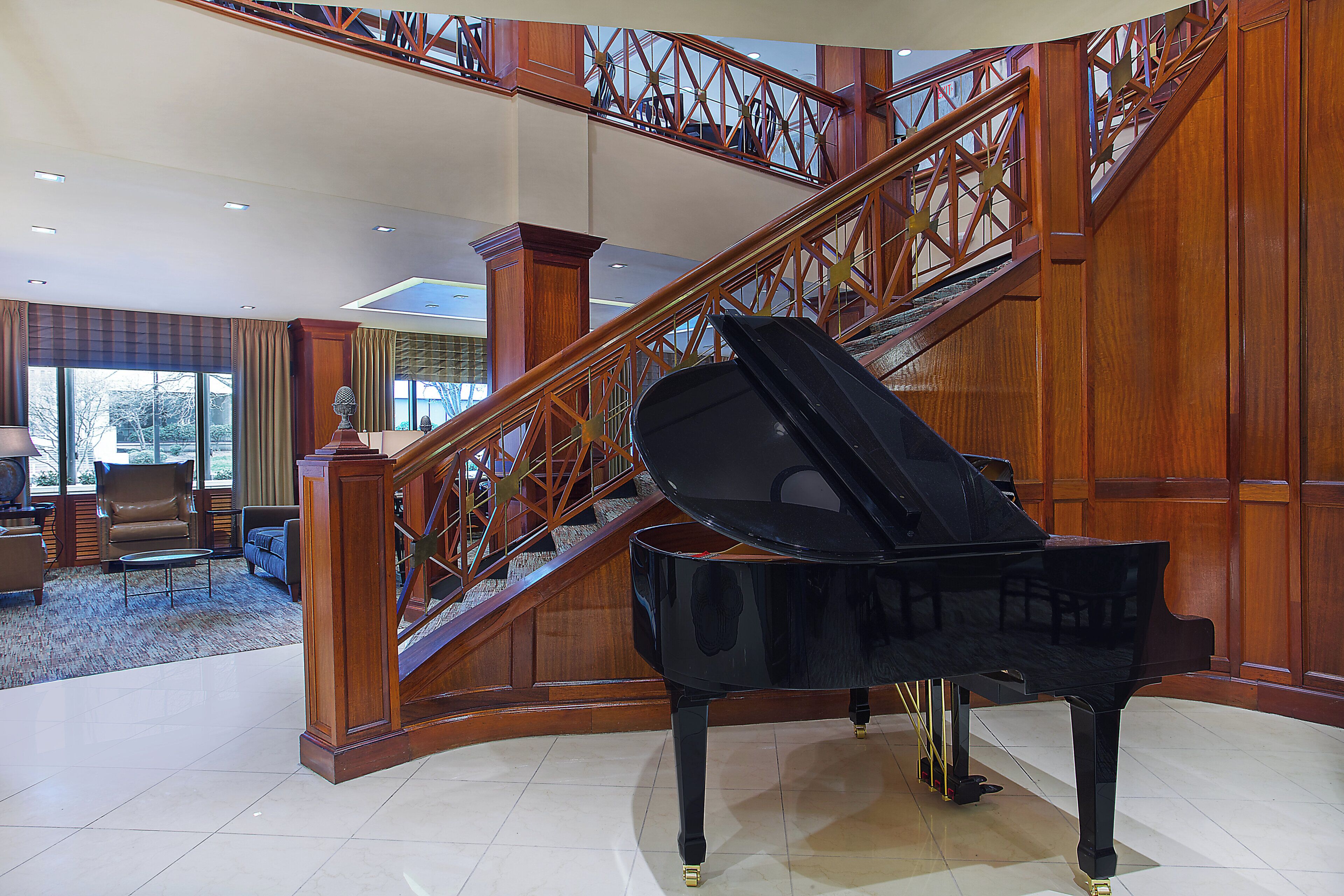 A grand piano in a spacious lobby with a wooden staircase and a view of the outdoors.