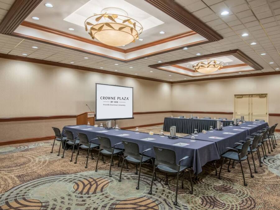 A conference room with a long table, chairs, a projector screen, and a carpeted floor.