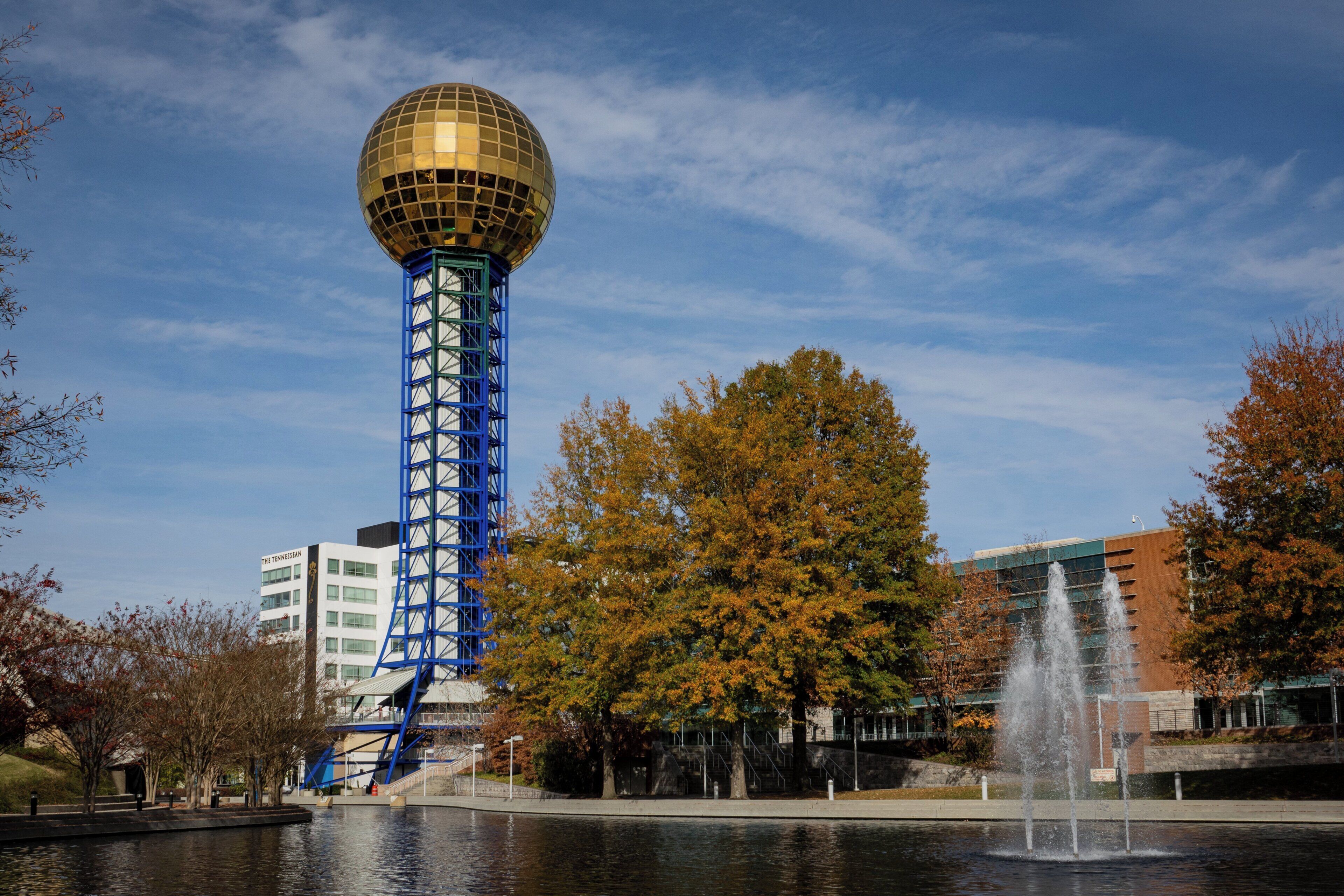 A tower with a spherical top, a fountain, and a body of water.