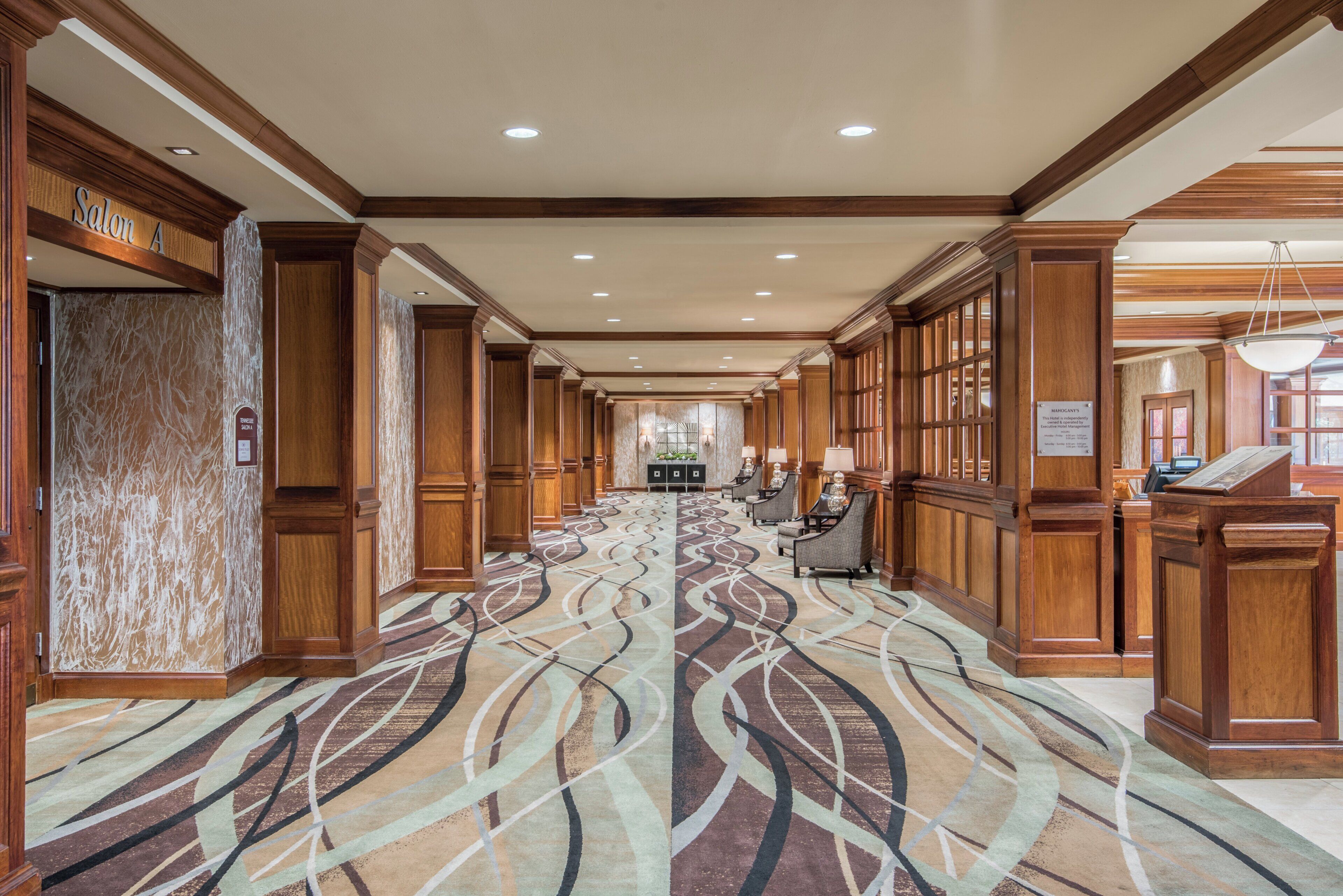 A hotel lobby with a patterned carpet, wooden paneling, and a reception desk.