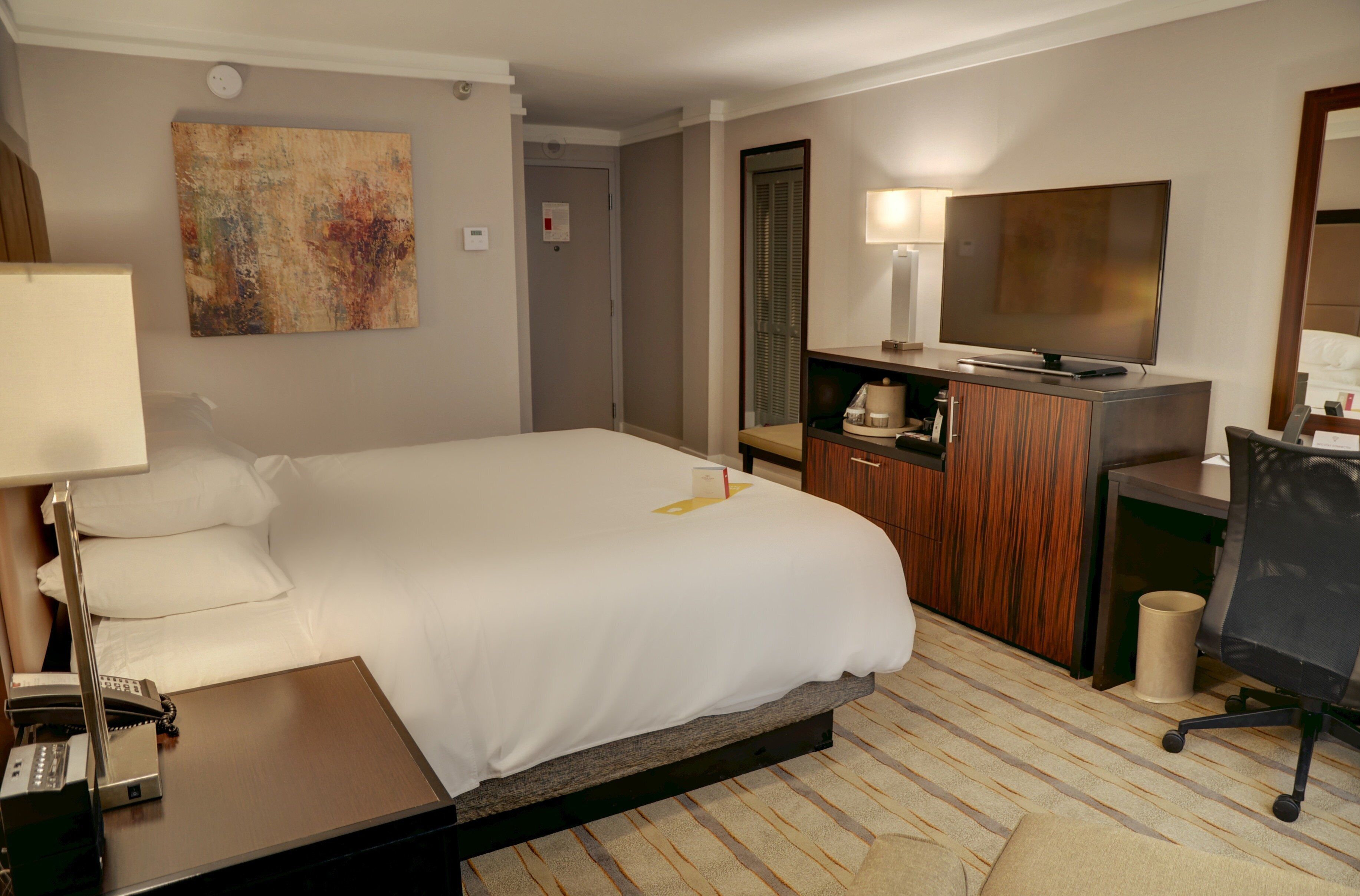 A hotel room with a large bed, a desk with a computer, a TV, and a painting on the wall.