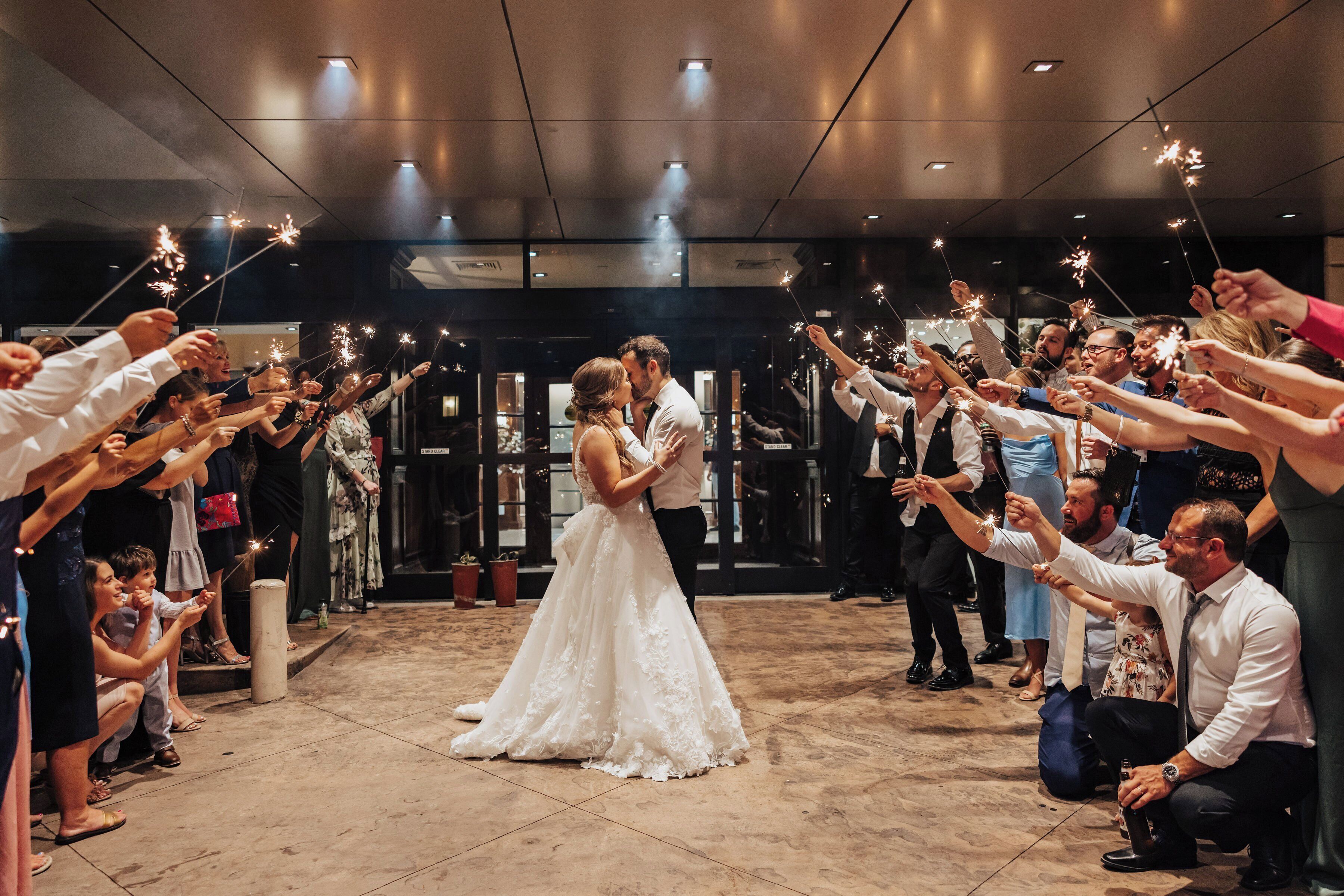 A wedding reception with guests holding sparklers, a bride in a white gown, and a groom in a suit.