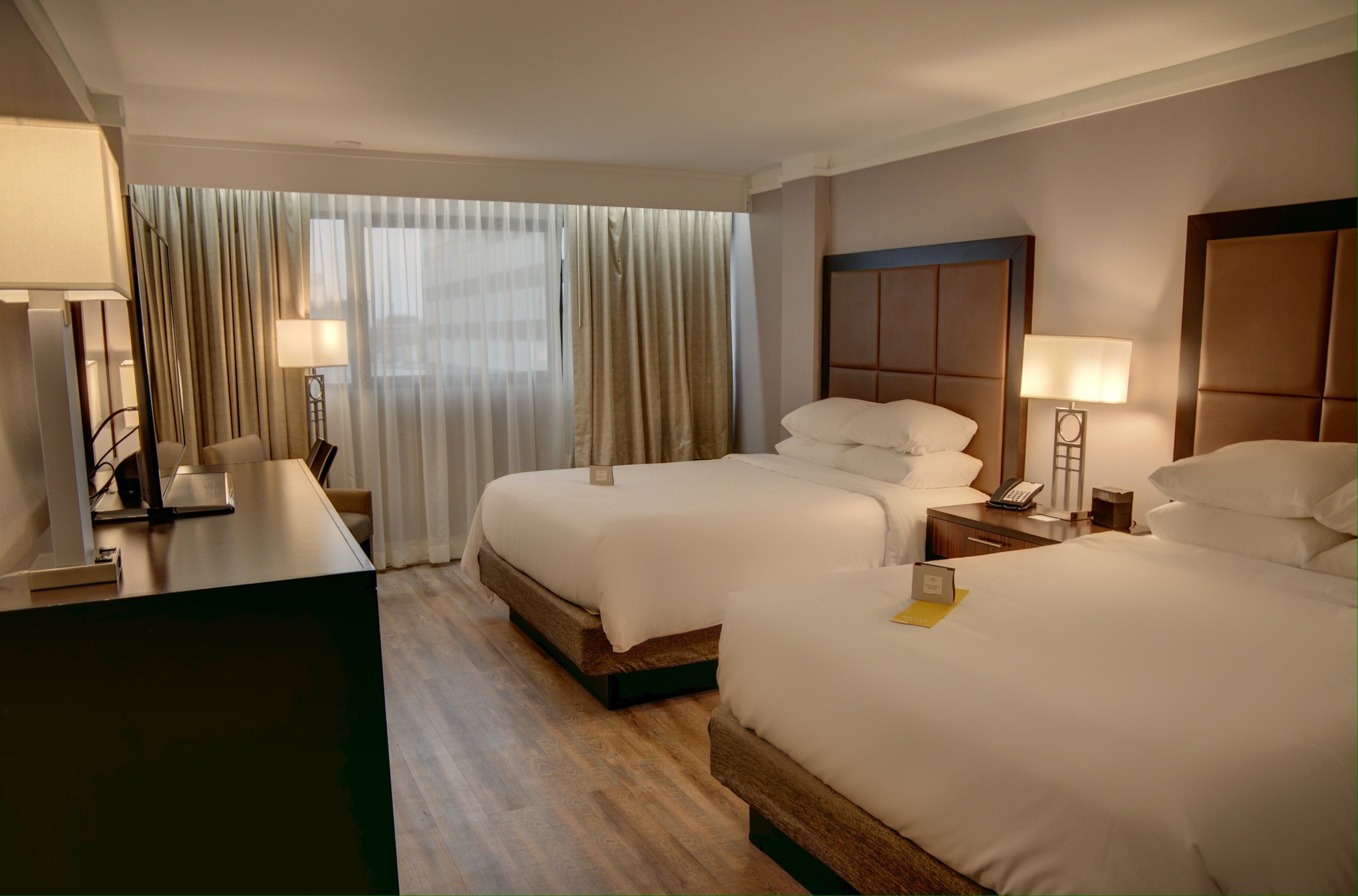 A hotel room with two beds, a desk, a chair, a telephone, and a window with curtains.