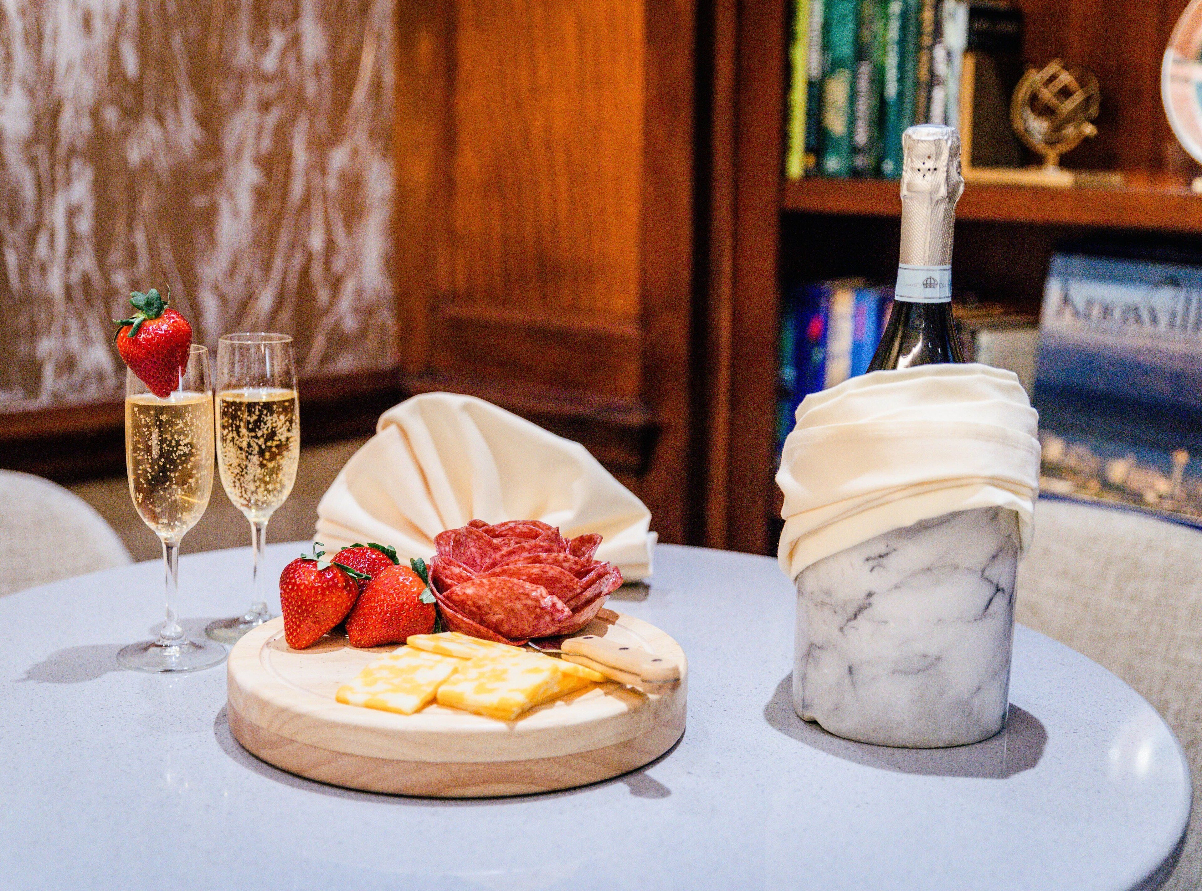 A table with two champagne flutes, a bottle of champagne, strawberries, and cheese on a marble surface.