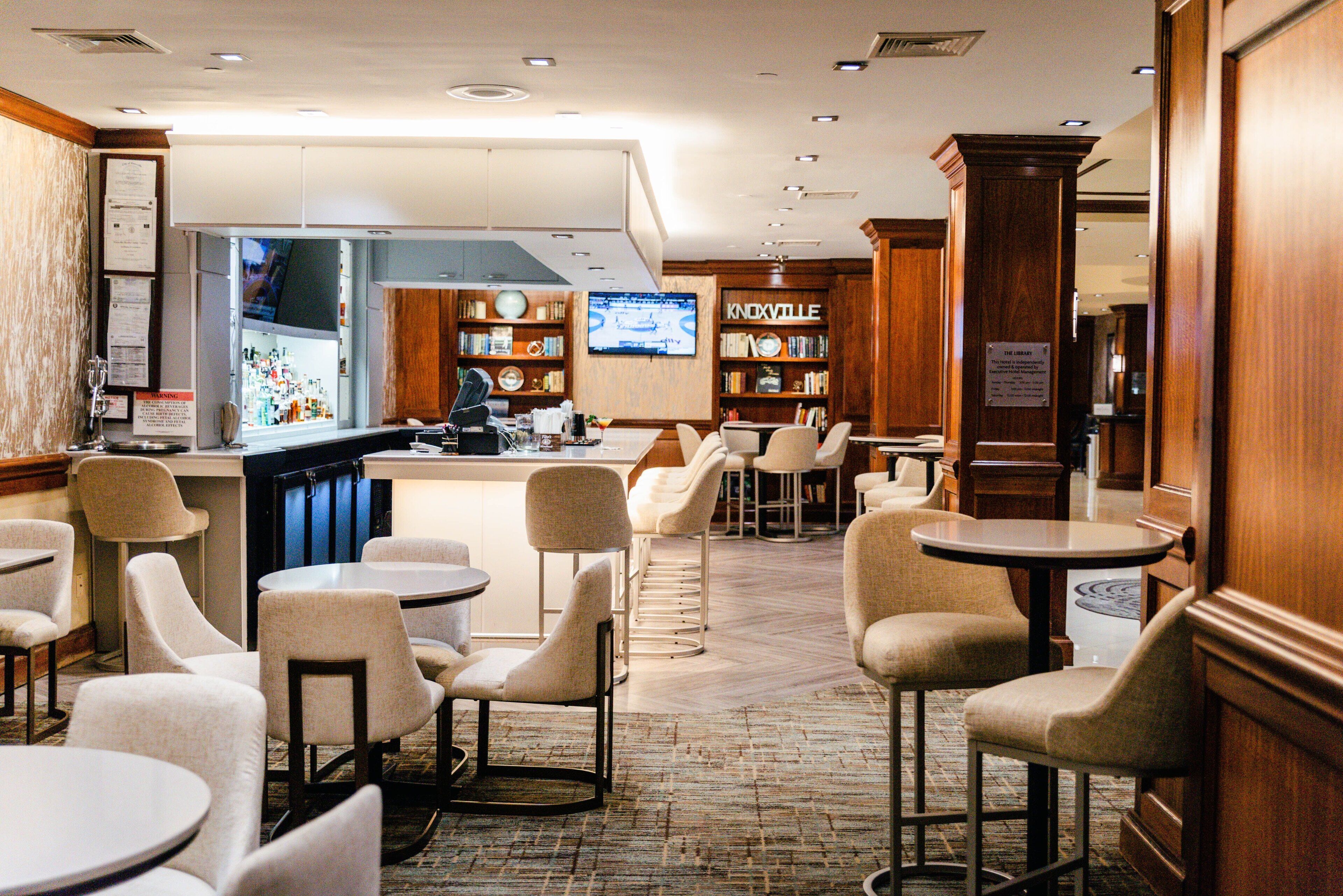 Un hall de hotel con una zona de bar, asientos y una pantalla de televisión.