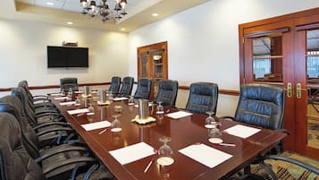 A conference room with a long table, multiple chairs, a flat-screen TV, and a chandelier.