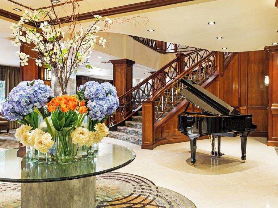 A grand lobby with a grand piano, a glass table with floral arrangements, and a staircase.