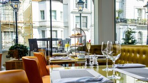 A dining area with a table set for two, chairs, and a view of the cityscape through large windows. - Blakemore Hyde Park (London)