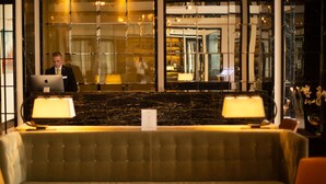 A hotel lobby with a marble reception desk, a seating area, and a large glass wall reflecting the interior. - Blakemore Hyde Park (London)