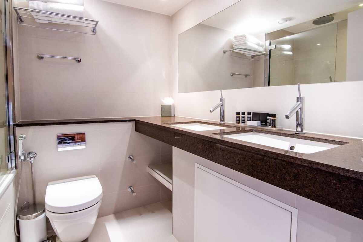 A modern bathroom with a double sink, a toilet, a shower, and a large mirror.