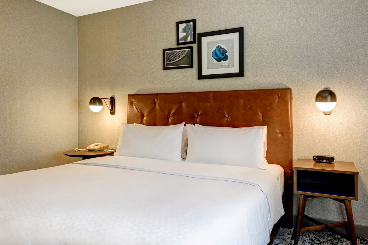 A hotel room with a large bed, a brown headboard, two bedside tables with lamps, and framed artwork on the wall.