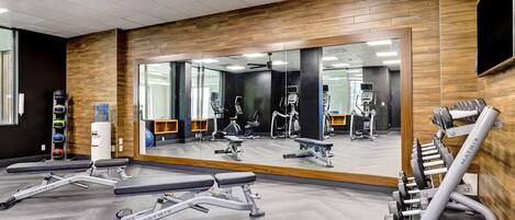 A gym with mirrored walls, exercise equipment, and a large mirror reflecting the space.