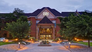 Entrada de un hotel con un letrero que dice "FOUR POINTS BY SHERATON" y un camino arbolado con luces.