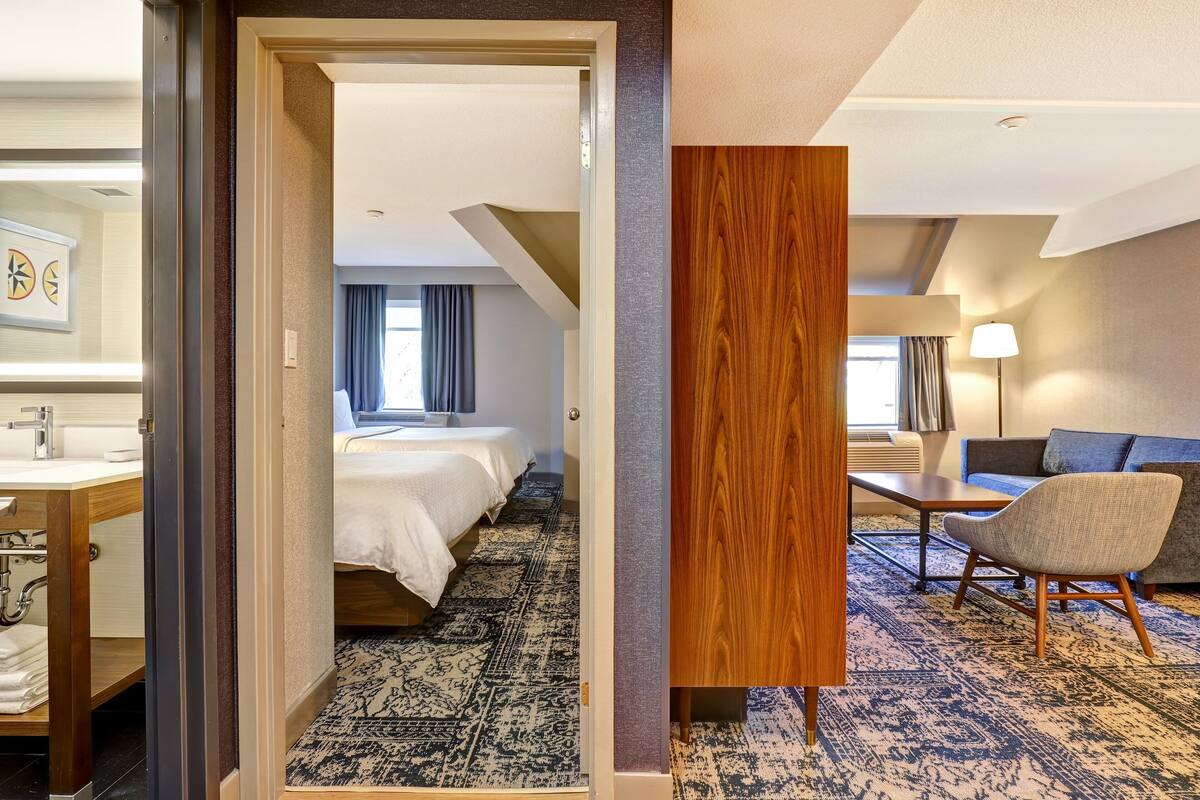 A hotel room with a bed, a desk, a chair, a bathroom, and a view of the outside.