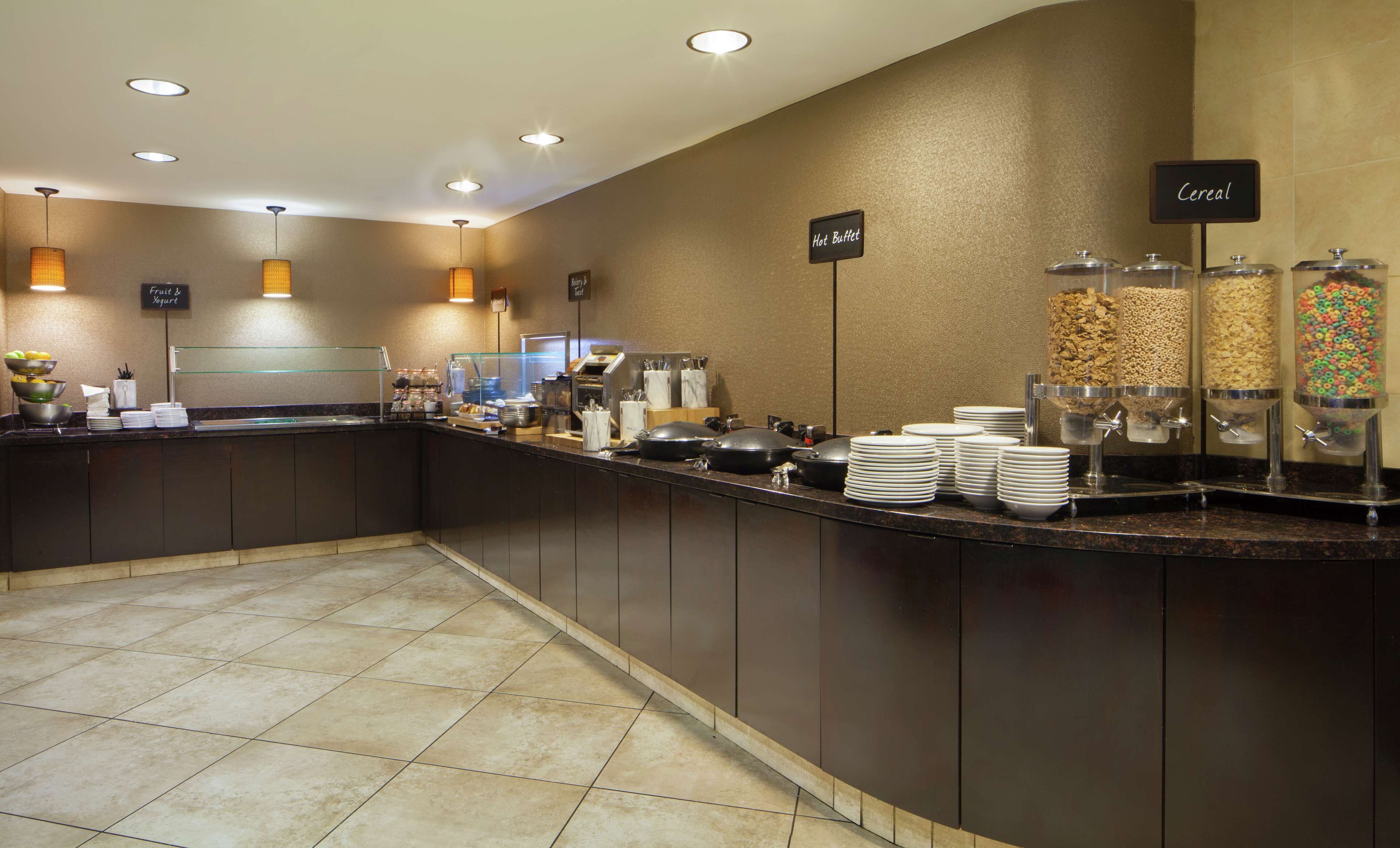 A hotel breakfast area with a self-serve station, including hot beverages, cereal, and yogurt.