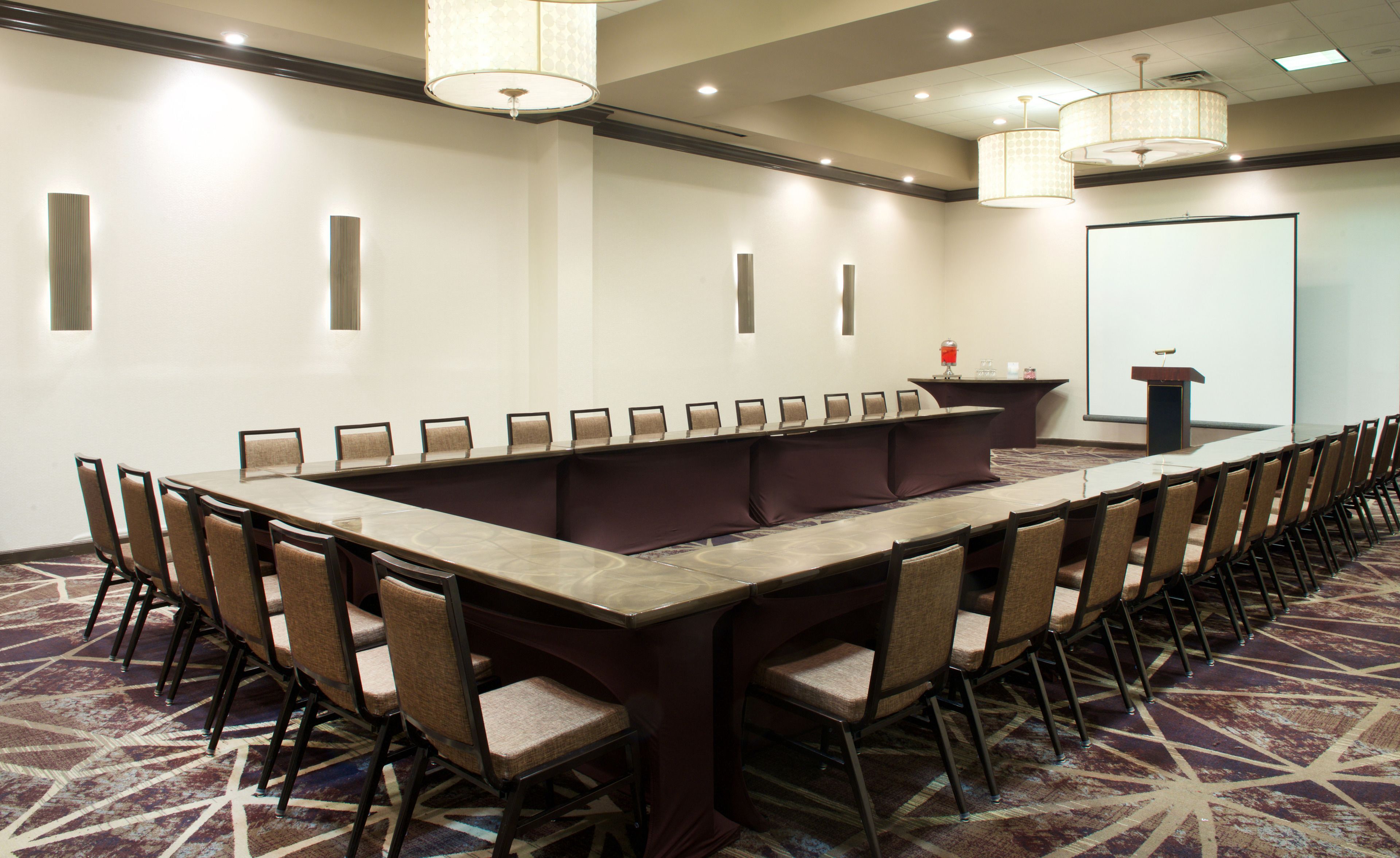 A conference room with a long table and chairs, a podium, and a projector screen.