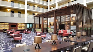 A hotel lobby with multiple seating areas, a central coffee table, and a large TV screen.