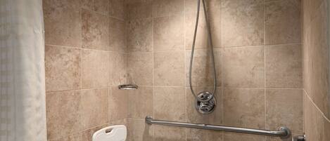 A bathroom with beige tiles, a shower with a handheld showerhead, a grab bar, and a white toilet.