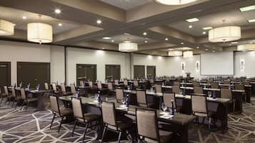 Une salle de conférence dotée de plusieurs tables et chaises, équipée de bouteilles d’eau et de documents, et un écran de projection fixé au mur.