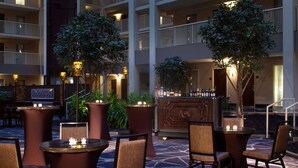An outdoor patio area with round tables and chairs, a bar with bottles, and a decorative cabinet.