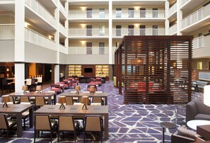 A hotel lobby with multiple floors, a central seating area with tables and chairs, a bar area, and a large wooden structure in the middle. - Embassy Suites by Hilton Philadelphia Airport (Philadelphia)