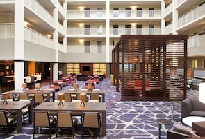 Un vestíbulo de hotel con varios pisos, un área de estar central con mesas y sillas, un área de bar y una gran estructura de madera en el centro.