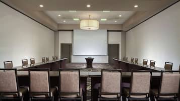 A conference room with a long table, chairs, a projector screen, and a chandelier.