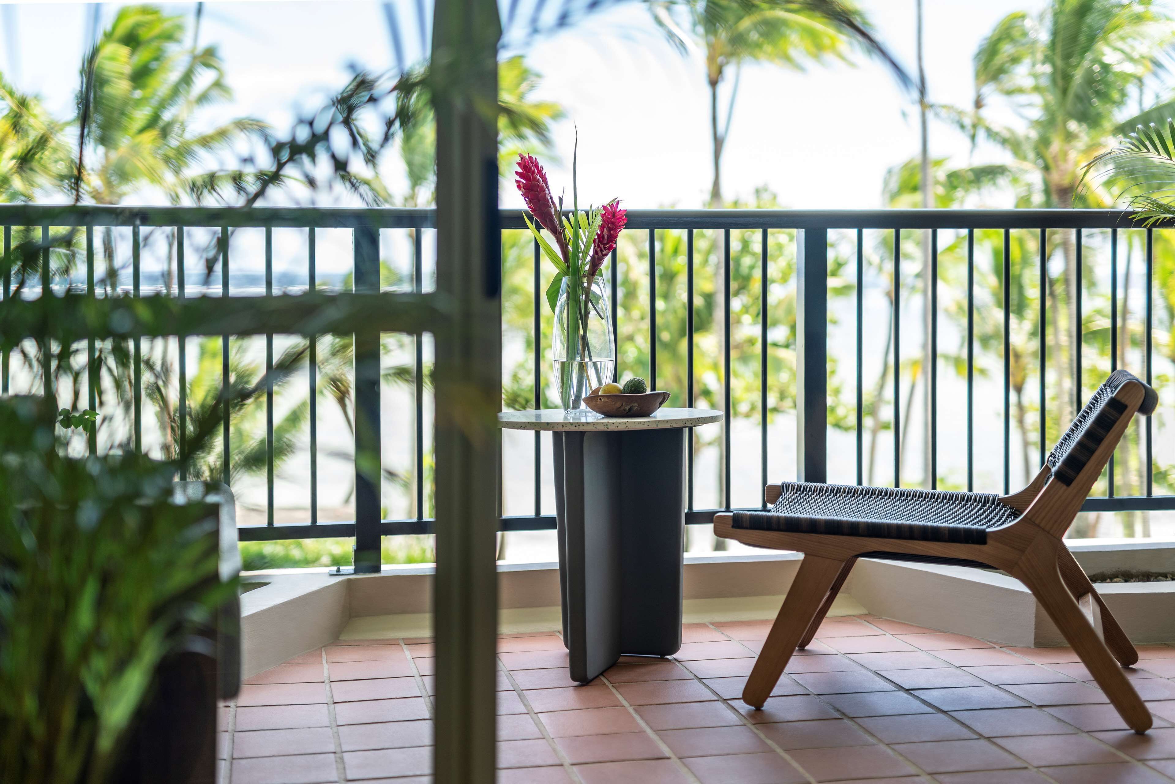 A balcony with a wooden chair and a small table with a vase of flowers.