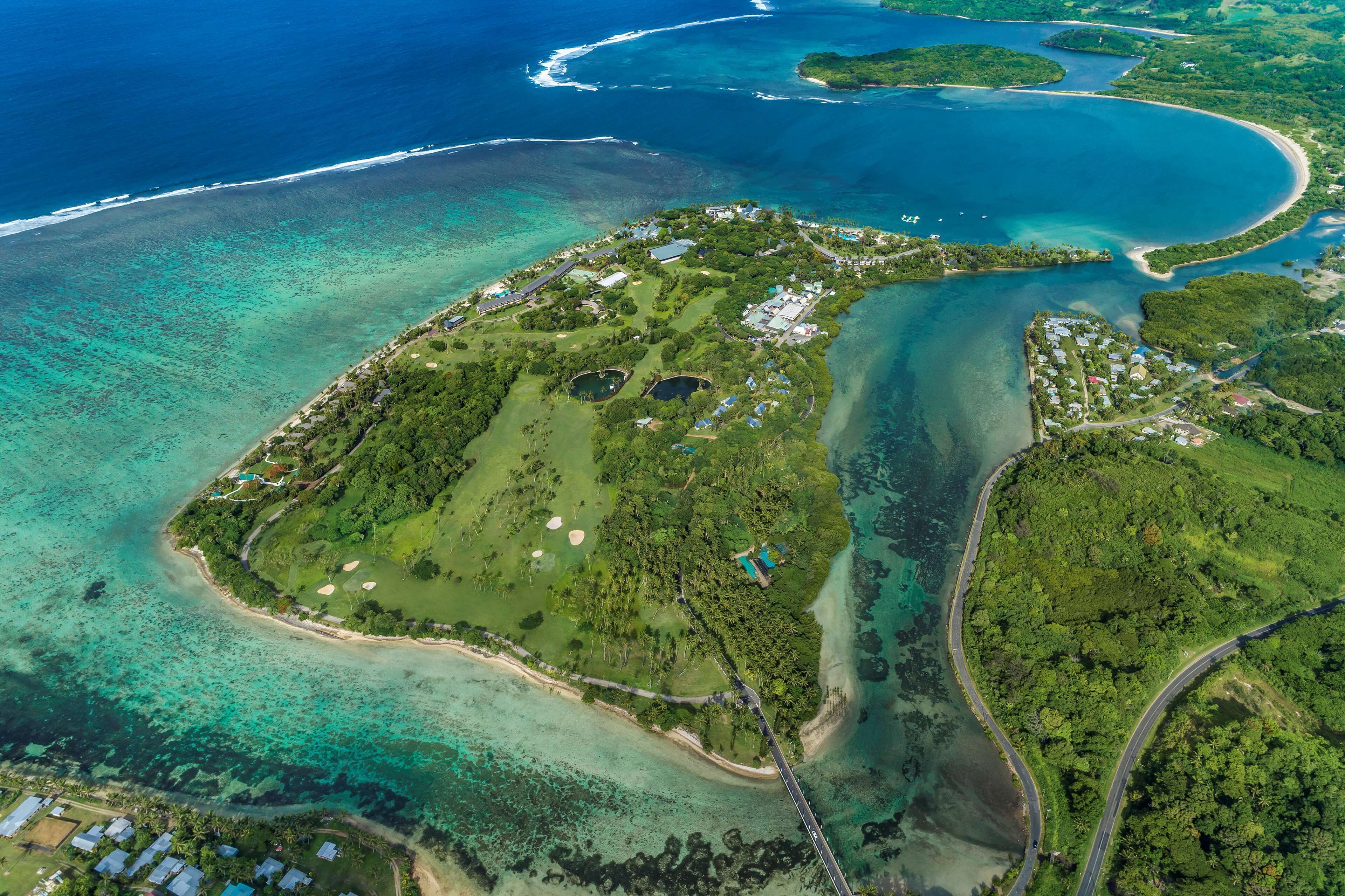 An aerial view of a coastal property with a golf course, clear blue waters, and a winding road.