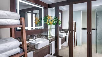 A modern bathroom with a vanity, a large mirror, a shower, and a glass door leading to another room.