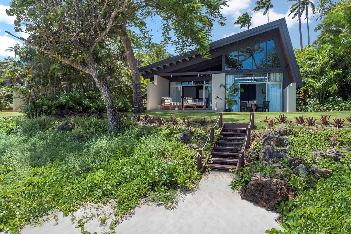 A modern house with a glass facade, a patio with outdoor furniture, and a stone pathway leading to the entrance.