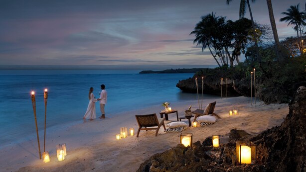 A beach setting with a couple walking, beach chairs, and lanterns. - Shangri-La Yanuca Island, Fiji (Yanuca Island)