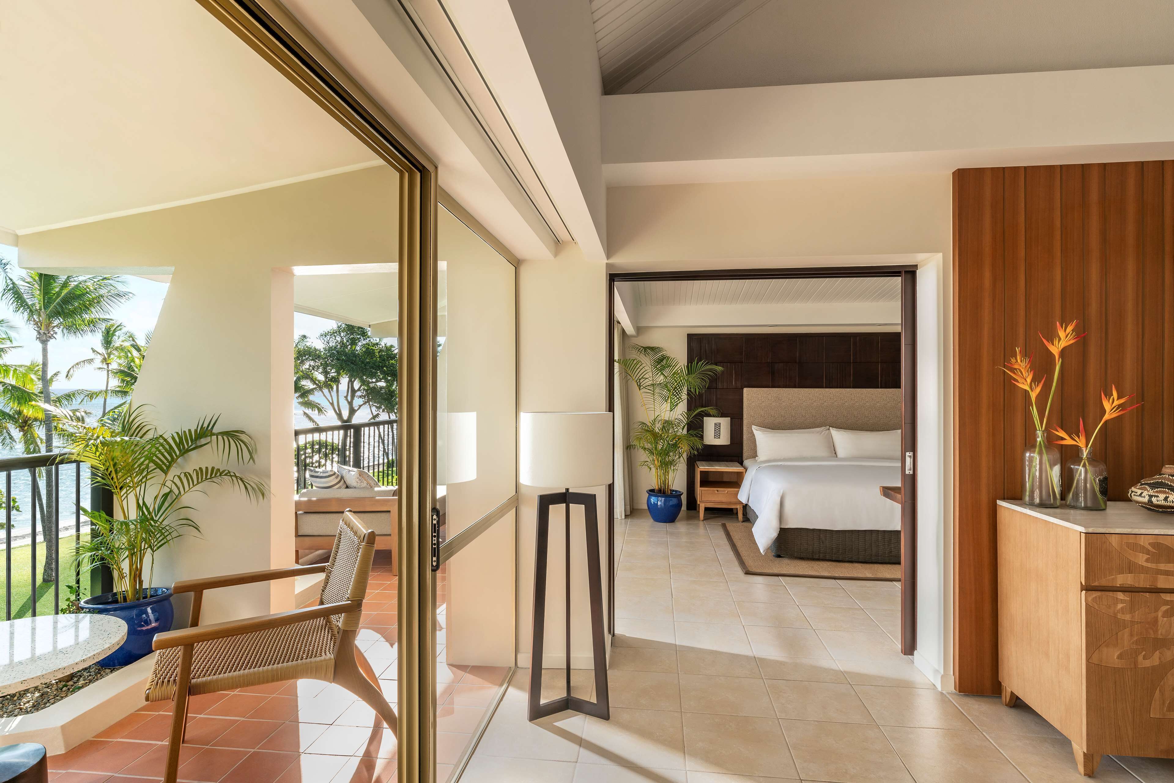 Habitación de hotel con balcón, cama, escritorio y una planta en maceta.