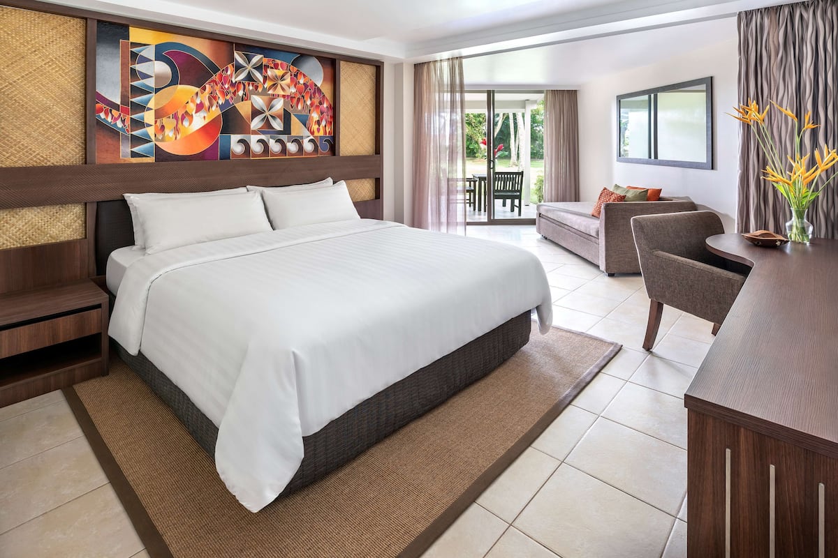 A hotel room with a large bed, a sofa, a dining table, and a view of the outdoors.
