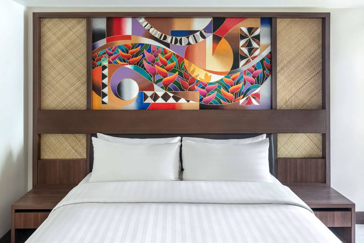 A hotel room with a large bed, two nightstands, and a colorful abstract artwork above the bed.