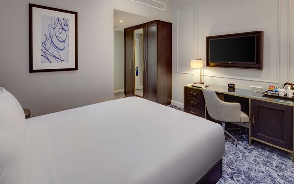 Habitación de hotel con una cama grande, un escritorio con una silla, un televisor y una obra de arte abstracta enmarcada en la pared.