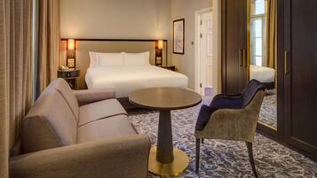 Une chambre d’hôtel avec un lit, un canapé, une chaise, une petite table ronde et un sol recouvert d’une moquette.